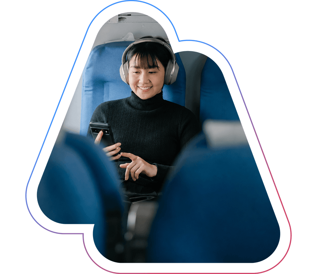 Person wearing headphones, smiling while using a smartphone, seated in a blue train seat.